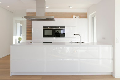 Photo of a medium sized contemporary single-wall kitchen/diner in Nuremberg with a submerged sink, flat-panel cabinets, white cabinets, grey splashback, stainless steel appliances, light hardwood flooring and an island.