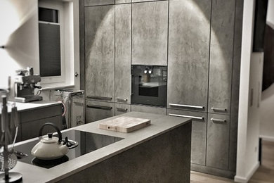 Offene, Kleine Moderne Küche in L-Form mit flächenbündigen Schrankfronten, grauen Schränken, schwarzen Elektrogeräten, braunem Holzboden, zwei Kücheninseln und braunem Boden in Köln