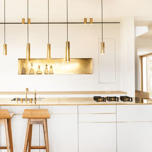 Zweizeilige, Offene, Kleine Moderne Küche mit Unterbauwaschbecken, flächenbündigen Schrankfronten, weißen Schränken, Küchenrückwand in Metallic, hellem Holzboden, Kücheninsel, beigem Boden und gelber Arbeitsplatte in München
