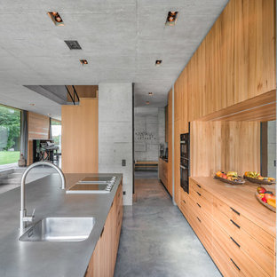 Zweizeilige Industrial Küche mit integriertem Waschbecken, flächenbündigen Schrankfronten, hellbraunen Holzschränken, Rückwand aus Spiegelfliesen, Betonboden, Kücheninsel, grauem Boden und grauer Arbeitsplatte in München