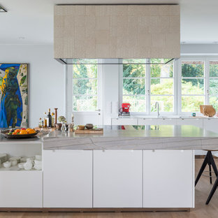 Offene, Zweizeilige, Große Moderne Küche mit flächenbündigen Schrankfronten, weißen Schränken, Küchengeräten aus Edelstahl, hellem Holzboden, Kücheninsel, braunem Boden, Marmor-Arbeitsplatte, Küchenrückwand in Weiß, Rückwand aus Holz und integriertem Waschbecken in Hamburg