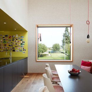 Modern inredning av ett stort linjärt kök med öppen planlösning, med en nedsänkt diskho, släta luckor, ljust trägolv, en halv köksö, svarta skåp och brunt golv