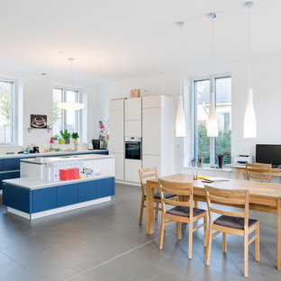 Offene, Große Moderne Küche in L-Form mit Waschbecken, Kassettenfronten, blauen Schränken, Porzellan-Bodenfliesen, Kücheninsel, grauem Boden und weißer Arbeitsplatte in Berlin