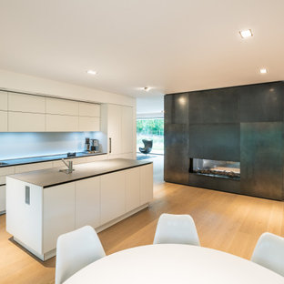 Offene, Zweizeilige Moderne Küche mit Unterbauwaschbecken, flächenbündigen Schrankfronten, weißen Schränken, Küchengeräten aus Edelstahl, hellem Holzboden, Kücheninsel, beigem Boden und grauer Arbeitsplatte in Frankfurt am Main