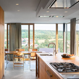Zweizeilige, Große Moderne Wohnküche mit Einbauwaschbecken, flächenbündigen Schrankfronten, Arbeitsplatte aus Holz, Küchengeräten aus Edelstahl, Porzellan-Bodenfliesen, Kücheninsel, grauem Boden, brauner Arbeitsplatte und hellbraunen Holzschränken in Sonstige