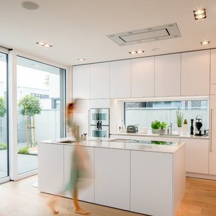 Offene, Zweizeilige, Große Moderne Küche mit Unterbauwaschbecken, flächenbündigen Schrankfronten, weißen Schränken, Mineralwerkstoff-Arbeitsplatte, Küchenrückwand in Weiß, Glasrückwand, weißen Elektrogeräten, braunem Holzboden, Kücheninsel, braunem Boden und weißer Arbeitsplatte in Düsseldorf