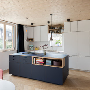 Zweizeilige Moderne Wohnküche mit Unterbauwaschbecken, flächenbündigen Schrankfronten, weißen Schränken, Küchenrückwand in Weiß, Elektrogeräten mit Frontblende, braunem Holzboden, Kücheninsel, braunem Boden und weißer Arbeitsplatte in München