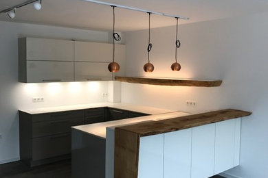 Inspiration for a medium sized contemporary u-shaped open plan kitchen in Hanover with a built-in sink, flat-panel cabinets, grey cabinets, engineered stone countertops, white splashback, black appliances, cement flooring, a breakfast bar and grey floors.