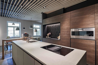Bild på ett stort funkis grå grått kök, med en undermonterad diskho, släta luckor, skåp i mörkt trä, bänkskiva i betong, svart stänkskydd, stänkskydd i cementkakel, rostfria vitvaror, en köksö och grått golv