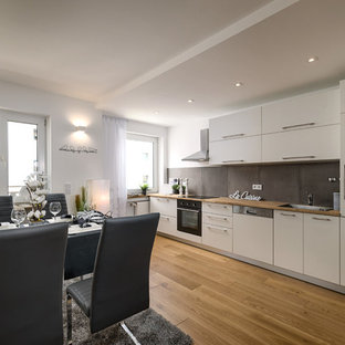 Mittelgroße, Einzeilige Moderne Wohnküche ohne Insel mit braunem Holzboden, braunem Boden, Einbauwaschbecken, flächenbündigen Schrankfronten, weißen Schränken, Arbeitsplatte aus Holz, Küchenrückwand in Schwarz, schwarzen Elektrogeräten und brauner Arbeitsplatte in München