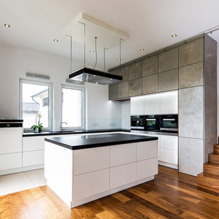 Moderne Küche in L-Form mit flächenbündigen Schrankfronten, grauen Schränken, Glasrückwand, schwarzen Elektrogeräten, braunem Holzboden, Kücheninsel, braunem Boden und schwarzer Arbeitsplatte in Hannover