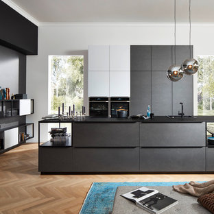 Offene, Zweizeilige, Große Industrial Küche mit Einbauwaschbecken, flächenbündigen Schrankfronten, schwarzen Schränken, schwarzen Elektrogeräten, hellem Holzboden, Kücheninsel, beigem Boden und schwarzer Arbeitsplatte in Hannover
