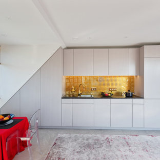 Moderne Küche mit Einbauwaschbecken, flächenbündigen Schrankfronten, weißen Schränken, Küchenrückwand in Metallic, Elektrogeräten mit Frontblende, grauem Boden und schwarzer Arbeitsplatte in München
