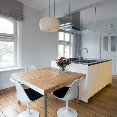 Example of a mid-sized trendy beige floor and medium tone wood floor open concept kitchen design in Hamburg with an integrated sink, flat-panel cabinets, white cabinets, an island and gray countertops