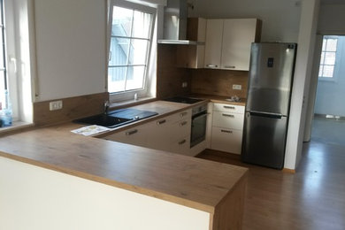 Mid-sized contemporary u-shaped open plan kitchen in Dusseldorf with a drop-in sink, flat-panel cabinets, laminate benchtops and a peninsula.