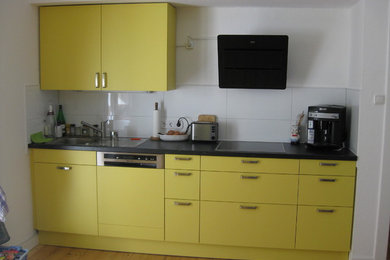 Photo of a mid-sized contemporary galley eat-in kitchen in Dusseldorf with a drop-in sink, laminate benchtops, white splashback, porcelain splashback, stainless steel appliances, medium hardwood floors, no island, flat-panel cabinets and yellow cabinets.