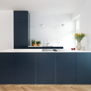 Moderne Küche in U-Form mit Unterbauwaschbecken, flächenbündigen Schrankfronten, blauen Schränken, hellem Holzboden, Halbinsel, beigem Boden und weißer Arbeitsplatte in Berlin