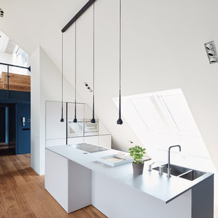 Große, Einzeilige Moderne Wohnküche mit integriertem Waschbecken, flächenbündigen Schrankfronten, weißen Schränken, braunem Holzboden, Kücheninsel, braunem Boden und Küchengeräten aus Edelstahl in Berlin