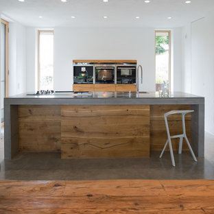 This is an example of a mid-sized contemporary open plan kitchen in Munich with an integrated sink, flat-panel cabinets, medium wood cabinets, concrete benchtops, white splashback, stainless steel appliances, concrete floors, with island, grey floor and grey benchtop.
