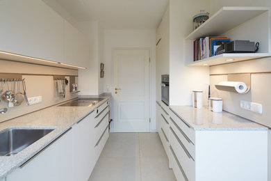 Moderne Küche mit Einbauwaschbecken, flächenbündigen Schrankfronten, weißen Schränken, Küchenrückwand in Weiß, Keramikboden und grauem Boden in München