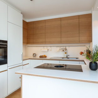 Offene, Mittelgroße Moderne Küche in U-Form mit Einbauwaschbecken, flächenbündigen Schrankfronten, weißen Schränken, Mineralwerkstoff-Arbeitsplatte, Küchenrückwand in Weiß, schwarzen Elektrogeräten, braunem Holzboden, Kücheninsel, braunem Boden, weißer Arbeitsplatte und eingelassener Decke in München