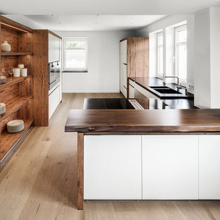 Imagen de cocina de galera, rústica, grande, abierta, con fregadero de doble seno, armarios con paneles lisos, puertas de armario blancas, encimera de madera, suelo de madera en tonos medios, península y salpicadero blanco
