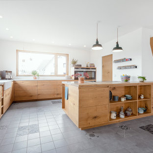 Offene, Große Moderne Küche in L-Form mit Landhausspüle, flächenbündigen Schrankfronten, Betonarbeitsplatte, schwarzen Elektrogeräten, Keramikboden, Kücheninsel, grauem Boden, hellbraunen Holzschränken und grauer Arbeitsplatte in Nürnberg