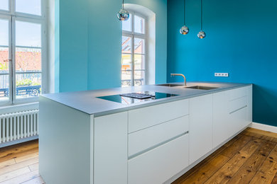 Moderne Wohnküche mit weißen Schränken, Edelstahl-Arbeitsplatte, braunem Holzboden und Kücheninsel in Sonstige