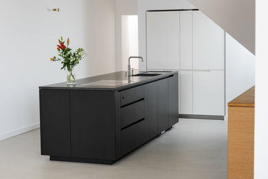 Immagine di una cucina moderna con ante nere, paraspruzzi bianco, elettrodomestici neri e pavimento in cemento