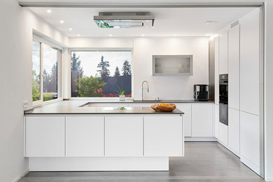 Moderne Küche mit flächenbündigen Schrankfronten, weißen Schränken, schwarzen Elektrogeräten, Betonboden, Kücheninsel und grauem Boden in Stuttgart