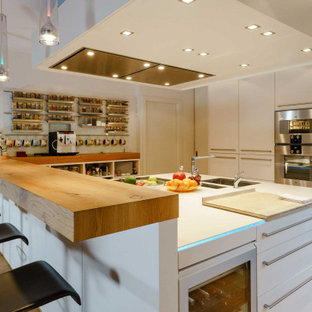 This is an example of a large modern open plan kitchen in Hamburg with an undermount sink, flat-panel cabinets, white cabinets, glass sheet splashback, medium hardwood floors, white benchtop and wallpaper.