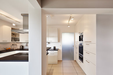 デュッセルドルフにあるコンテンポラリースタイルのおしゃれなアイランドキッチン (フラットパネル扉のキャビネット、白いキャビネット、白いキッチンパネル、シルバーの調理設備、テラコッタタイルの床) の写真