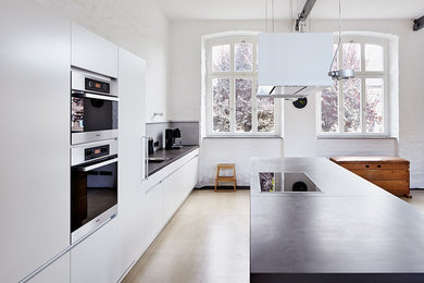 デュッセルドルフにある広いコンテンポラリースタイルのおしゃれなキッチン (フラットパネル扉のキャビネット、白いキャビネット、白いキッチンパネル、ガラス板のキッチンパネル、シルバーの調理設備) の写真