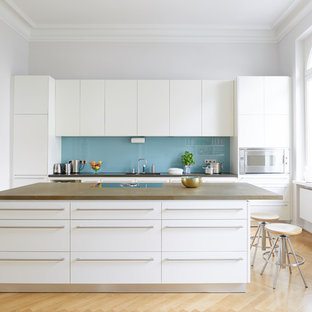 Geschlossene, Große, Zweizeilige Klassische Küche mit flächenbündigen Schrankfronten, weißen Schränken, Glasrückwand, Küchengeräten aus Edelstahl, hellem Holzboden, brauner Arbeitsplatte, Küchenrückwand in Blau, Kücheninsel und beigem Boden in Bonn