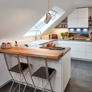 Mittelgroße Moderne Wohnküche ohne Insel in U-Form mit Unterbauwaschbecken, flächenbündigen Schrankfronten, weißen Schränken, Arbeitsplatte aus Fliesen, Küchenrückwand in Weiß, Glasrückwand, schwarzen Elektrogeräten, Keramikboden, grünem Boden und grauer Arbeitsplatte in Dortmund