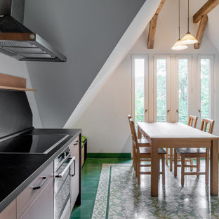 Photo of a large country galley eat-in kitchen in Other with an integrated sink, flat-panel cabinets, light wood cabinets, solid surface benchtops, black splashback, slate splashback, stainless steel appliances, porcelain floors, no island, green floor and black benchtop.
