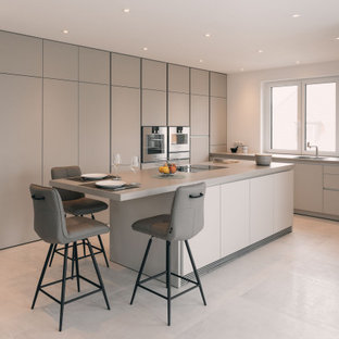 Moderne Küche in L-Form mit Unterbauwaschbecken, flächenbündigen Schrankfronten, grauen Schränken, Küchengeräten aus Edelstahl, Kücheninsel, grauem Boden und grauer Arbeitsplatte in Nürnberg