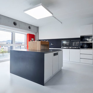 Geschlossene, Einzeilige, Mittelgroße Moderne Küche mit flächenbündigen Schrankfronten, weißen Schränken, Küchenrückwand in Schwarz, schwarzen Elektrogeräten, Betonboden, Kücheninsel, grauem Boden und schwarzer Arbeitsplatte in Sonstige