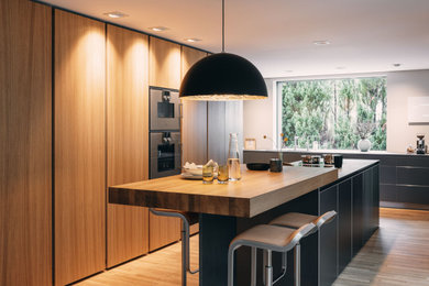 Moderne Küche in L-Form mit flächenbündigen Schrankfronten, grauen Schränken, Arbeitsplatte aus Holz, Küchengeräten aus Edelstahl, braunem Holzboden, Kücheninsel, braunem Boden und brauner Arbeitsplatte in Nürnberg