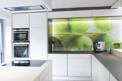 Mittelgroße Moderne Küche mit flächenbündigen Schrankfronten, weißen Schränken, Glas-Arbeitsplatte, Glasrückwand, Küchengeräten aus Edelstahl und Kücheninsel in Frankfurt am Main