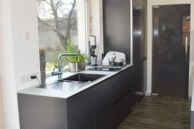 Offene Moderne Küche mit integriertem Waschbecken, grauen Schränken, Glas-Arbeitsplatte, Porzellan-Bodenfliesen, Kücheninsel und weißer Arbeitsplatte in Sonstige