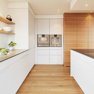 Moderne Küche in U-Form mit integriertem Waschbecken, flächenbündigen Schrankfronten, weißen Schränken, Küchenrückwand in Weiß, Küchengeräten aus Edelstahl, braunem Holzboden, Kücheninsel, braunem Boden und grauer Arbeitsplatte in Stuttgart