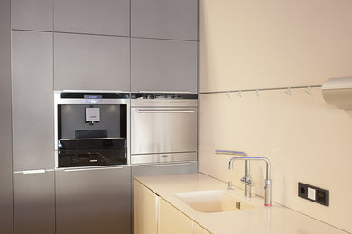 Moderne Küche mit integriertem Waschbecken, flächenbündigen Schrankfronten, grauen Schränken, Küchenrückwand in Weiß, Glasrückwand und Küchengeräten aus Edelstahl in Frankfurt am Main