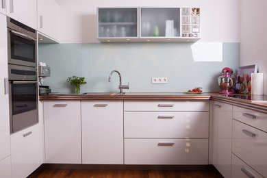 Kleine Moderne Küche mit weißen Schränken und Glasrückwand in Hamburg