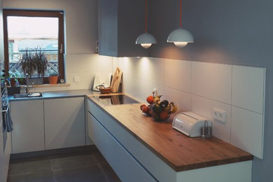 Offene Skandinavische Küche ohne Insel in U-Form mit integriertem Waschbecken, Edelstahl-Arbeitsplatte, Rückwand aus Porzellanfliesen und schwarzen Elektrogeräten in München