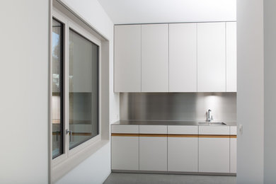 Moderne Küche mit flächenbündigen Schrankfronten, weißen Schränken und Edelstahl-Arbeitsplatte in Sonstige