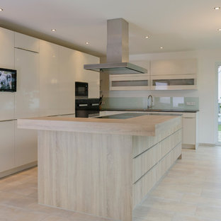 Idee per un'ampia cucina design con ante lisce, ante bianche, top in legno, paraspruzzi bianco, paraspruzzi con lastra di vetro, elettrodomestici in acciaio inossidabile, isola e pavimento in pietra calcarea