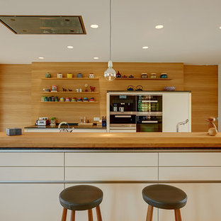 Foto di una grande cucina abitabile contemporanea con ante lisce, ante bianche, isola, paraspruzzi marrone, elettrodomestici in acciaio inossidabile e parquet chiaro