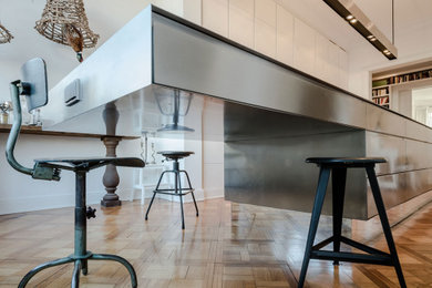Offene, Zweizeilige, Große Moderne Küche mit flächenbündigen Schrankfronten, weißen Schränken, Edelstahl-Arbeitsplatte, braunem Holzboden und Kücheninsel in Hamburg