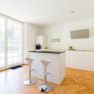 Moderne Küche in L-Form mit flächenbündigen Schrankfronten, weißen Schränken, braunem Holzboden, Kücheninsel, braunem Boden und beiger Arbeitsplatte in Essen